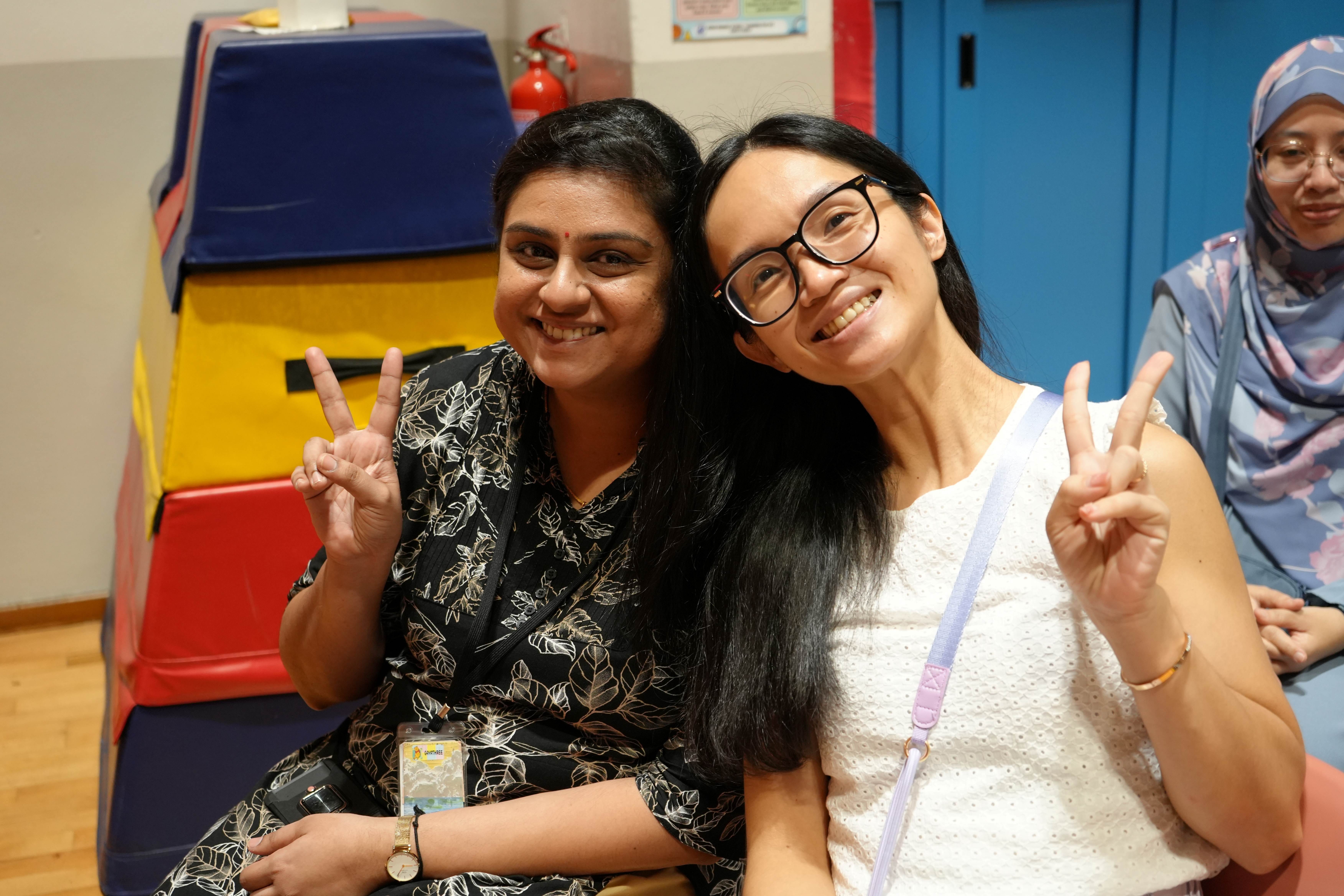 Two teachers smile and flash peace signs for the camera.